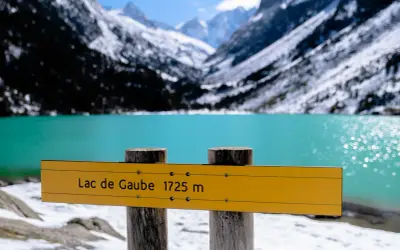 Panneau jaune indiquant "Lac de Gaube 1725 m" devant un lac turquoise et des montagnes enneigées.