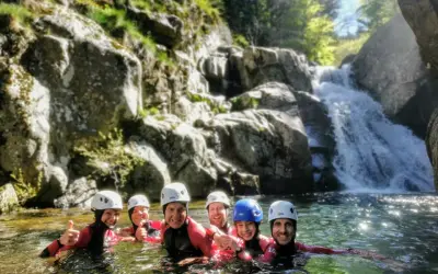 Groupe souriant en combinaison néoprène, casques blancs et bleus, profitant d'une descente en canyoning près d'une cascade. Une belle aventure de canyoning dans le Vallon Pont d'Arc.