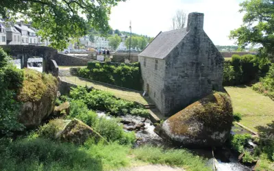 Un ancien bâtiment en pierre près d'un ruisseau, avec des rochers moussus. On dirait la grotte du diable, un lieu mystérieux.