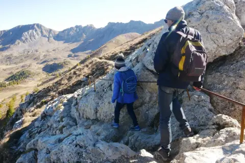 Deux randonneurs escaladent un sentier rocheux dans le cirque de Morgon, avec des montagnes escarpées en arrière-plan.