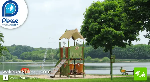 Aire de jeux près de l'étang de Buhel, avec un toboggan et un portique. Le logo WakePark Plessé est visible.