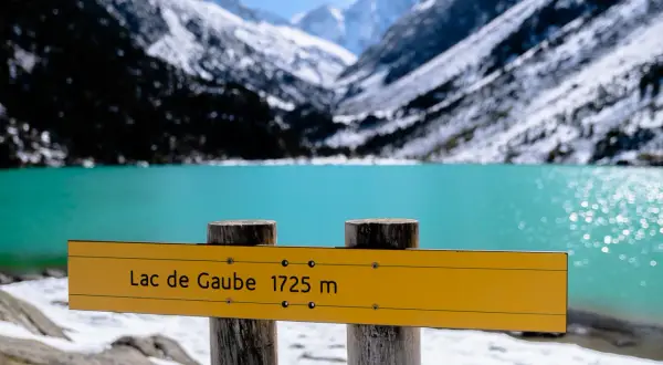 Panneau jaune indiquant "Lac de Gaube 1725 m" devant un lac turquoise et des montagnes enneigées.