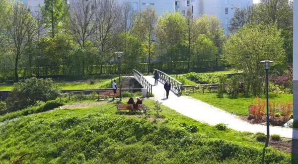 Promenade paisible aux prairies Saint-Martin à Rennes, avec un pont traversant un cours d'eau et des résidents profitant du soleil sur des bancs.