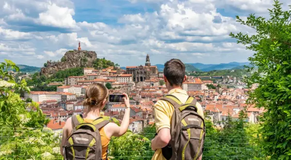Couple avec sacs à dos admire la vue panoramique du Puy-en-Velay, capturant le moment pour immortaliser leur visite à pied.