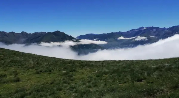 Vue panoramique depuis le col de Riou, avec des montagnes verdoyantes émergeant d'une mer de nuages sous un ciel bleu éclatant.