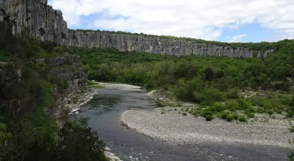 Rivière serpentant dans un cirque de falaises calcaires, le cirque de gens ruoms, bordé de verdure luxuriante.