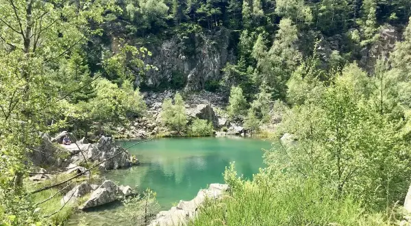 Un paisible lac bleu en Haute-Loire, entouré de rochers et d'une forêt verdoyante.