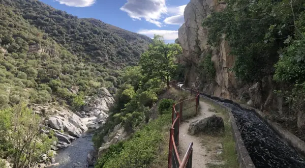 Sentier longeant un canal d'eau vive dans les gorges de la Guillera, avec une rivière en contrebas et des montagnes verdoyantes.