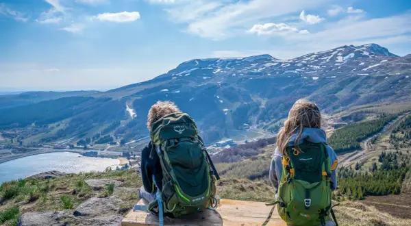 Deux randonneurs contemplent le paysage depuis le Puy de Chambourguet. Le lac scintille, les montagnes enneigées se dressent à l'horizon.