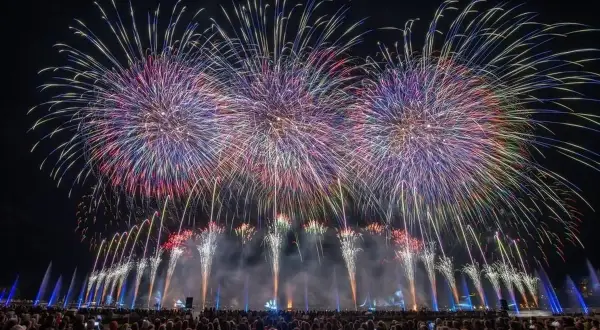 Spectacle de feu d'artifice sur le lac d'Annecy, illuminant le ciel nocturne de gerbes colorées au-dessus d'une foule admirative.