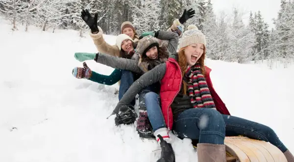 Des amis s'amusent en luge dans la neige, une scène joyeuse typique d'Annecy en décembre.