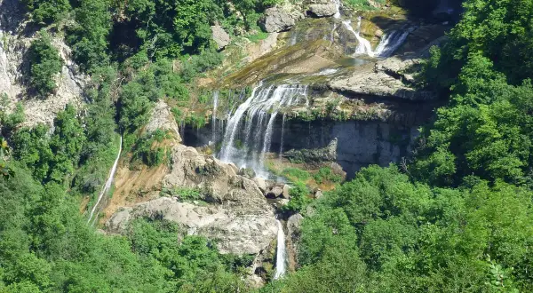 La cascade de la Charabotte dévale une falaise rocheuse, entourée d'une végétation luxuriante. L'eau forme de multiples bras sur les rochers.