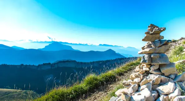 Un cairn de pierres marque le sommet, offrant une vue panoramique sur la grande sure et les montagnes bleutées à perte de vue sous un ciel clair.