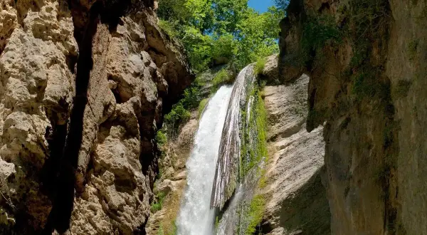 La chute de la druise, une cascade spectaculaire, dévale une falaise rocheuse verdoyante, entourée par la végétation luxuriante et le ciel bleu.