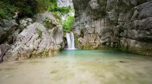 Cascade d'eau tombant dans un bassin turquoise au cœur de la gorge du Nan, entourée de falaises rocheuses et de végétation luxuriante.