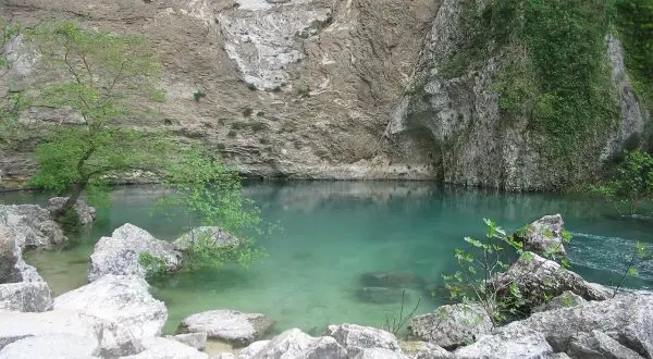 Le gouffre de la Fontaine de Vaucluse, une eau turquoise limpide émergeant d'une falaise rocheuse, entourée de végétation luxuriante et de rochers.