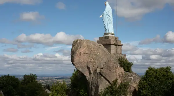 Statue de la Vierge sur la butte de Suin, veillant sur la vallée sous un ciel bleu parsemé de nuages.
