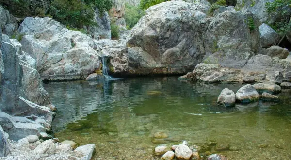 Un petit bassin d'eau claire aux Gorges d'Héric, avec une cascade tombant entre des rochers massifs. Une carte naturelle de ce lieu paisible.