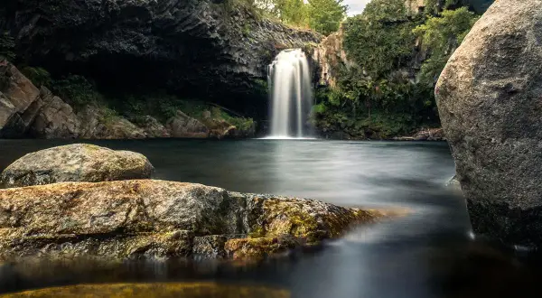 Magnifique cascade piscine naturelle en Ardèche, entourée de rochers et de végétation luxuriante. L'eau tombe en voile blanc dans le bassin sombre.