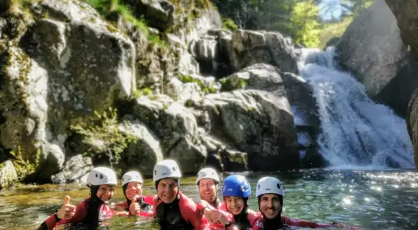 Groupe souriant en combinaison néoprène, casques blancs et bleus, profitant d'une descente en canyoning près d'une cascade. Une belle aventure de canyoning dans le Vallon Pont d'Arc.