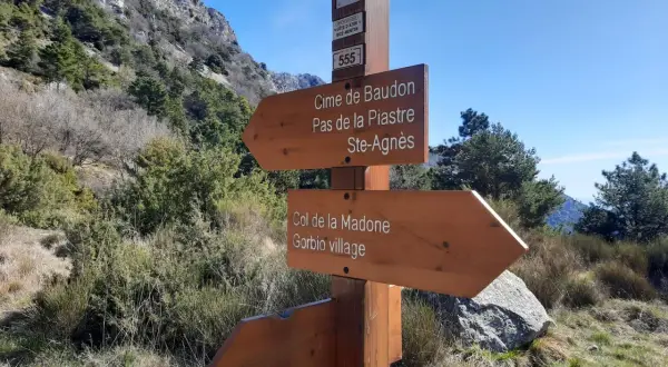 Panneau indicateur de randonnée : direction Cime de Baudon, Pas de la Piastre, Ste-Agnès, Col de la Madone et Gorbio village. Paysage montagneux.