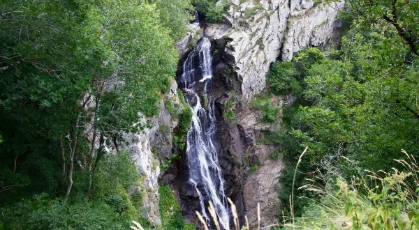 La cascade de Cubserviès dévale une falaise rocheuse, entourée d'une végétation luxuriante. L'eau blanche contraste avec le sombre des rochers.