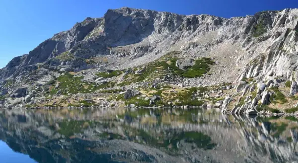Reflets parfaits des montagnes rocheuses sur le lac de Bastani, sous un ciel bleu éclatant.