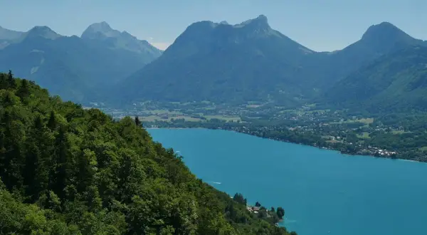 Vue panoramique du lac d'Annecy, ses eaux turquoise bordées de montagnes verdoyantes. Idéal pour un tour du lac Annecy en km.