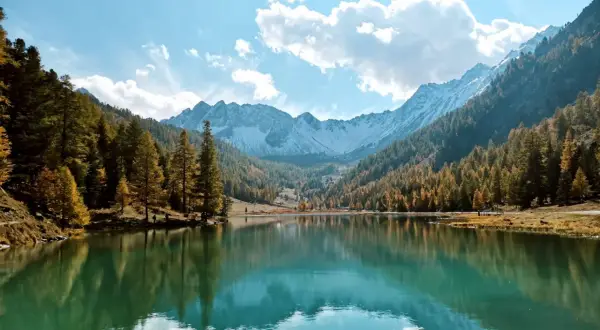 Le lac de l'Orceyrette, miroir des montagnes enneigées et des forêts d'automne, sous un ciel bleu éclatant.