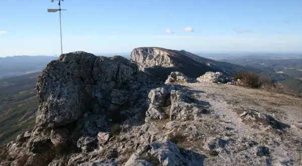 Vue panoramique depuis le pic des mouches, avec un anémomètre sur un rocher et un paysage de montagnes et de vallées sous un ciel bleu.