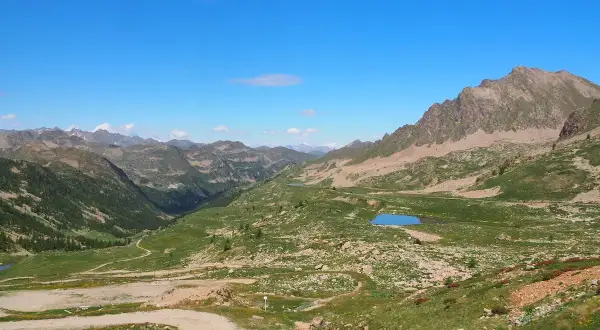 Vue panoramique du col de la Lombarde, avec des montagnes verdoyantes, des lacs bleus et un ciel clair.