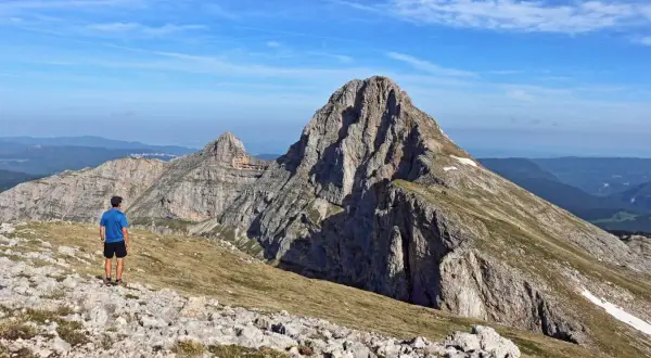 Un randonneur admire la majesté de la grande moucherolle, un pic rocheux imposant sous un ciel bleu.
