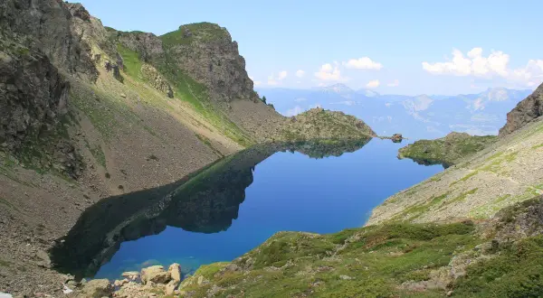 Le lac du Crozet, d'un bleu profond, reflète les montagnes escarpées et le ciel clair. Un paysage alpin paisible.