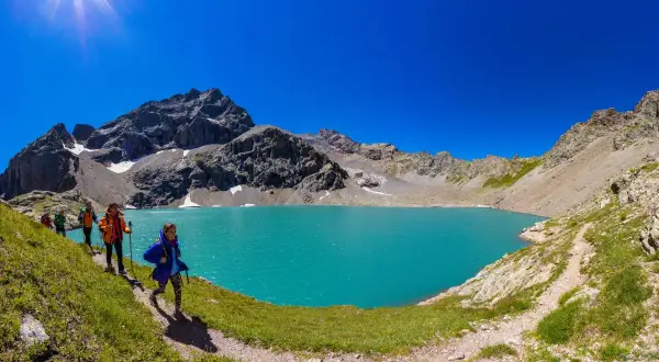 Randonneurs découvrant le magnifique lac de l'Eychauda, aux eaux turquoise vives, sous un ciel d'azur éclatant.