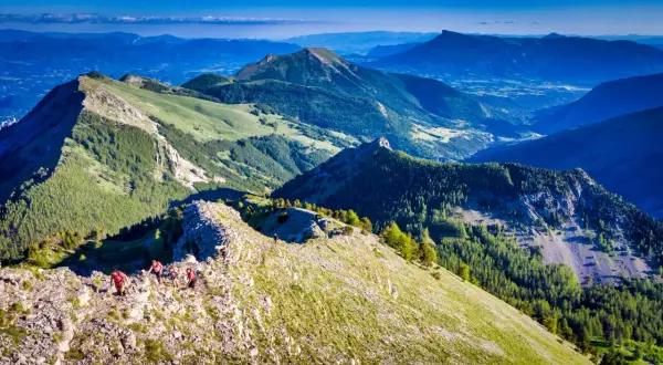 Randonneurs sur la crête rocheuse menant au pic de Gleize, avec des montagnes verdoyantes et un ciel bleu.