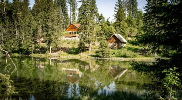 Reflets parfaits des chalets et des sapins dans le lac du Poursollet, un paysage de montagne paisible.