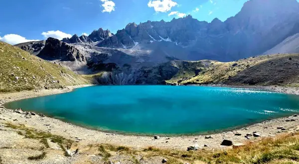 Magnifique lac Saint-Anne aux eaux turquoise, entouré de montagnes rocheuses et de pentes herbeuses sous un ciel bleu éclatant.
