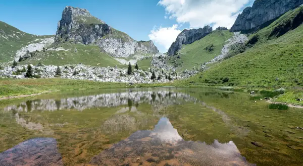 Le lac de Darbon, paisible, reflète les montagnes verdoyantes et rocheuses sous un ciel bleu et nuageux.
