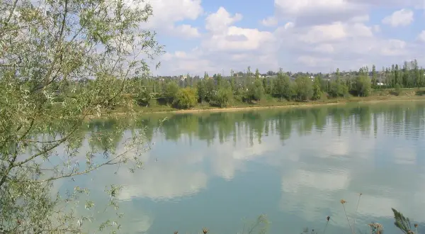 Le lac de Beaupuy, paisible sous un ciel bleu parsemé de nuages blancs, reflète la végétation luxuriante de ses rives.