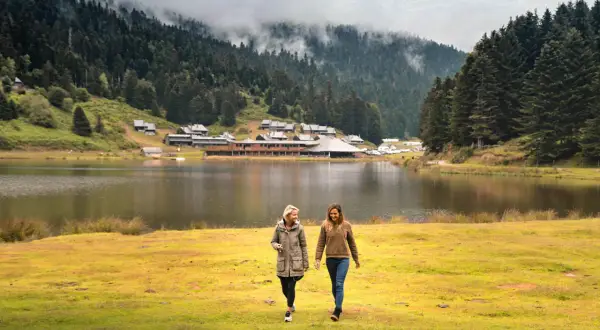 Deux amies profitent d'une promenade au bord du lac de Payolle, entouré de forêts et de montagnes brumeuses.