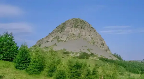 Le rocher de Sampzon, imposant et rocheux, se dresse sous un ciel bleu. Des arbres verts l'entourent.
