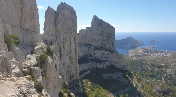 Vue spectaculaire depuis le pas de la demi lune, avec des falaises calcaires imposantes dominant la mer Méditerranée et un village côtier.
