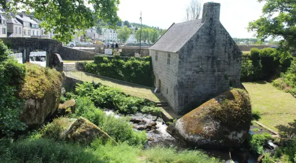 Un ancien bâtiment en pierre près d'un ruisseau, avec des rochers moussus. On dirait la grotte du diable, un lieu mystérieux.