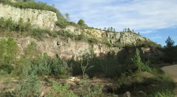 Falaises rocheuses verdoyantes sous un ciel bleu, évoquant le **Puy de Naouri**. Végétation dense au premier plan.