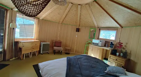 Intérieur douillet d'une yourte au col du Festre, avec un lit confortable, une kitchenette et une vue sur la nature.