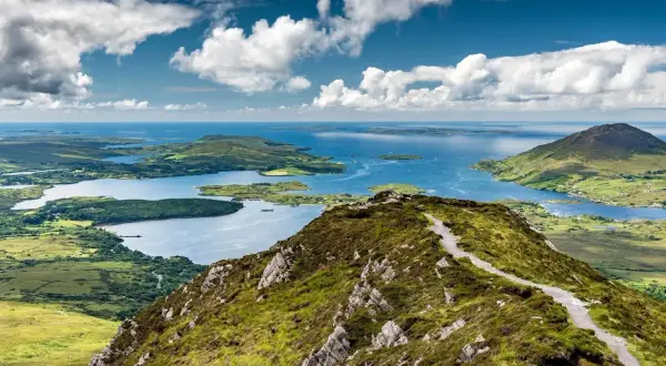 Vue panoramique du lac du Connemara, un lieu d'une beauté sauvage avec des montagnes verdoyantes et des eaux bleues scintillantes sous un ciel nuageux.