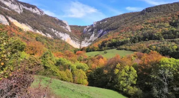 Vallée automnale aux couleurs vives, menant à la cascade de Chaudeyrolles. Le ciel bleu contraste avec les falaises et les arbres aux teintes orangées et vertes.