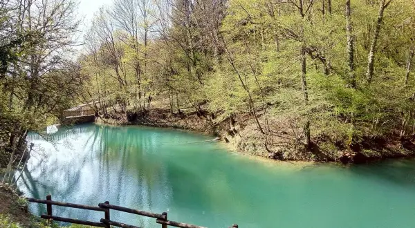 Le lac bleu d'Amberieu, une eau turquoise limpide bordée d'arbres verdoyants et d'un pont en bois.