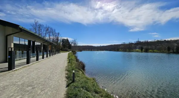 Promenade paisible au bord du lac de Flourens, avec un bâtiment moderne et un ciel bleu éclatant.
