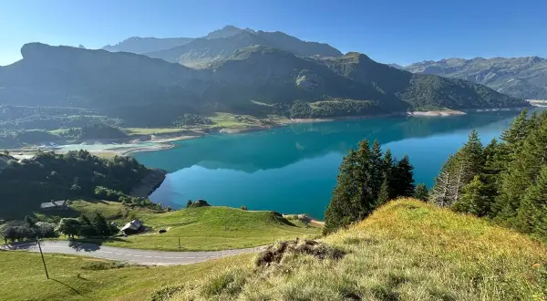 Vue panoramique du lac de la Gittaz aux eaux turquoise, entouré de montagnes verdoyantes et d'une route sinueuse.
